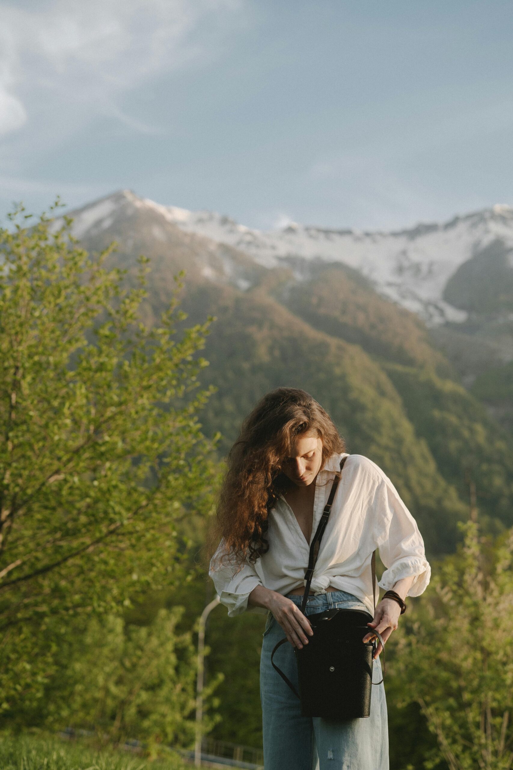 A fashionable woman in white top and jeans stands in a scenic mountain landscape, enjoying the outdoors.